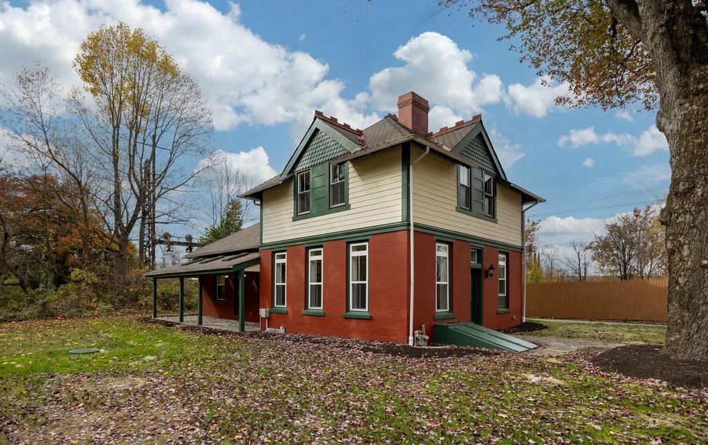 Two-story cream and red house with a porch, surrounded by autumn trees and fallen leaves.