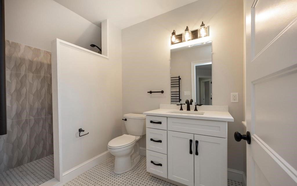 Bright bathroom with white vanity, toilet, shower curtain, and large mirror with lights.