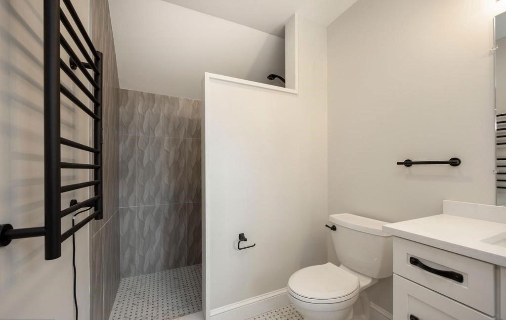 Modern white bathroom with toilet, vanity, towel rack, and tiled shower stall