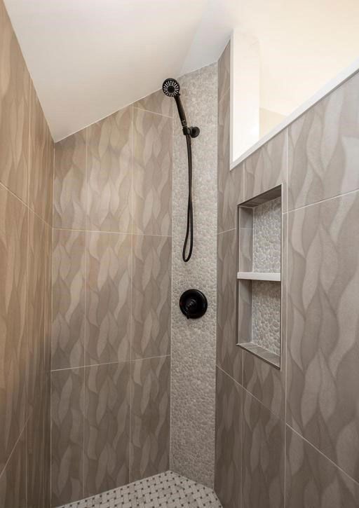 Small tiled shower with patterned beige walls, black showerhead, and built-in corner shelves.