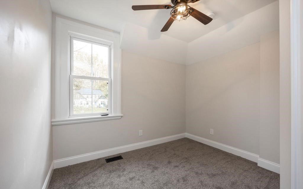Empty beige bedroom with a window, carpeted floor, and a ceiling fan.