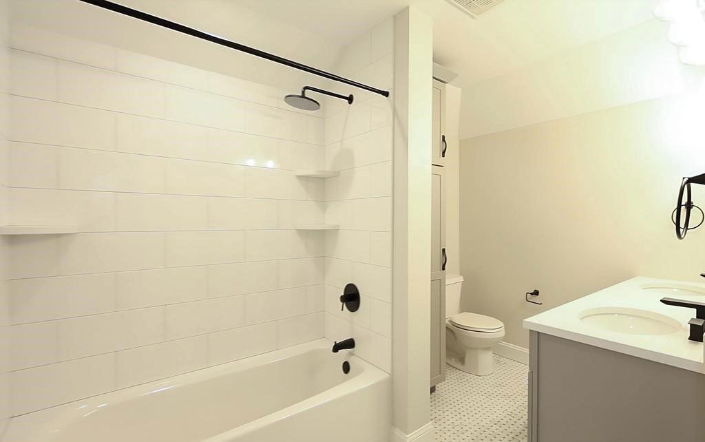 Bright white bathroom with a bathtub, shower curtain rod, toilet, and sink counter.