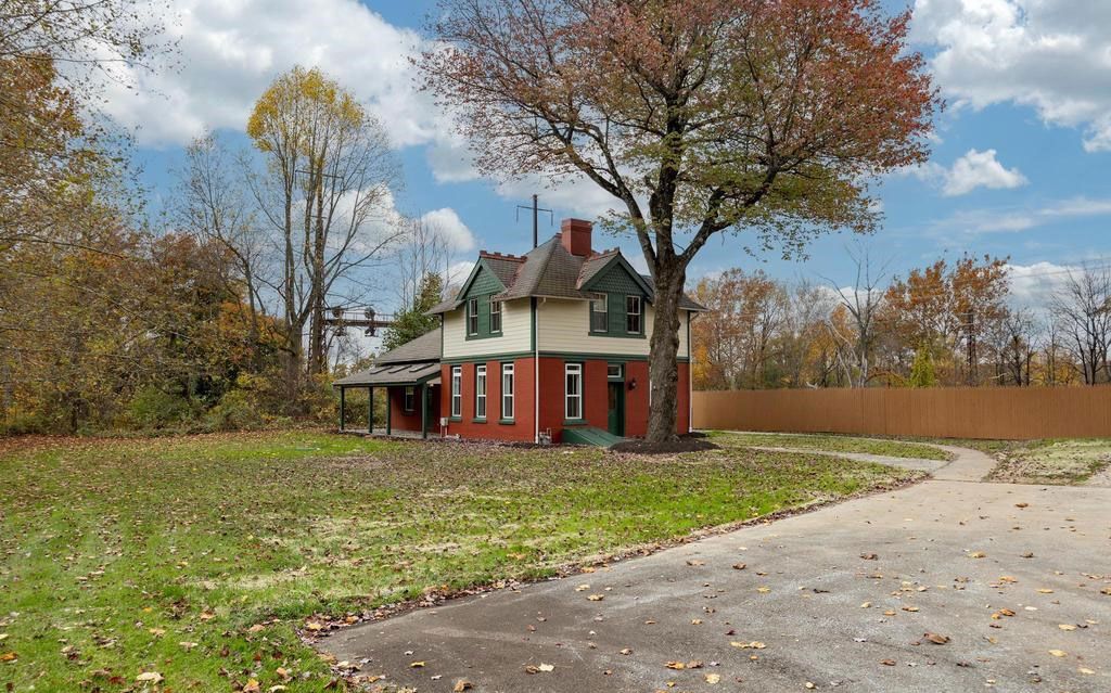 Small red house beside a curved road in autumn with bare trees and cloudy sky
