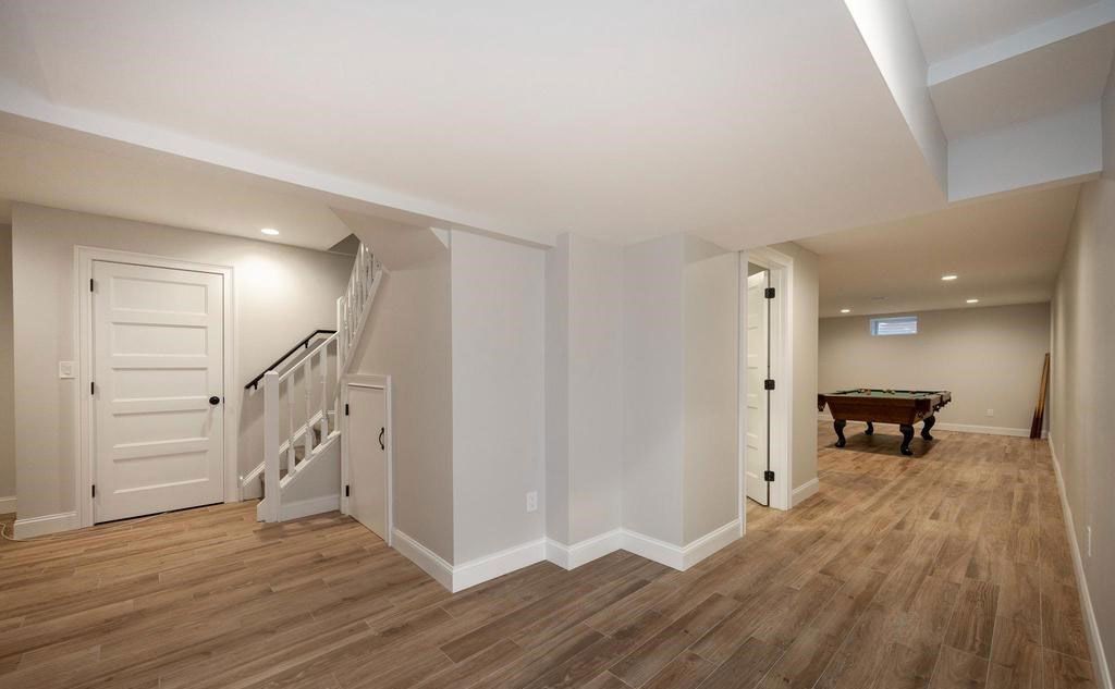 Finished basement rec room with wood floors, staircase, white doors, and a pool table in the back.