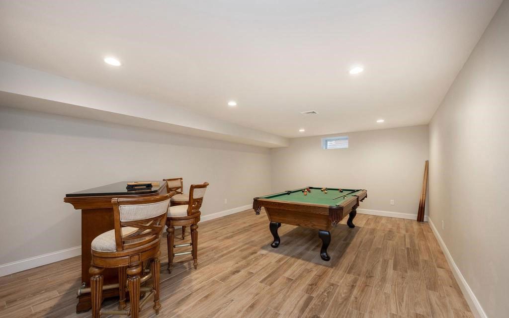 Basement rec room with a pool table, bar, and wood flooring under recessed lights