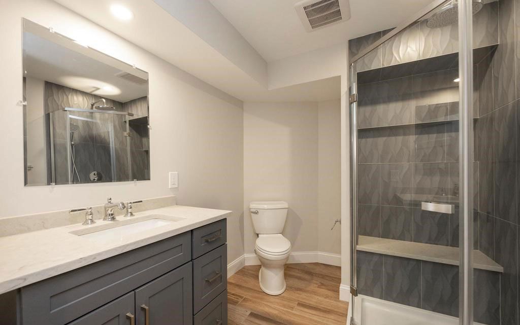 Modern bathroom with dark vanity, white countertop, toilet, mirror, and gray shower curtain.