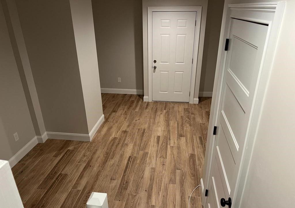 Empty hallway with wood-look flooring, beige walls, and a white front door.