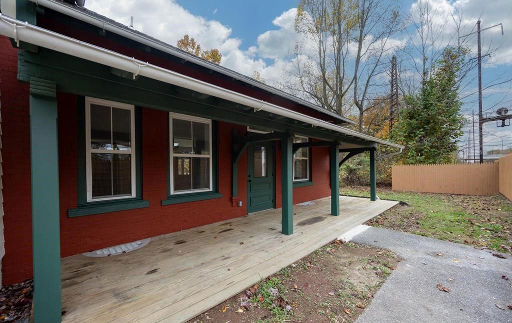 Single-story red building with green trim, covered porch, and gravel path under a cloudy sky