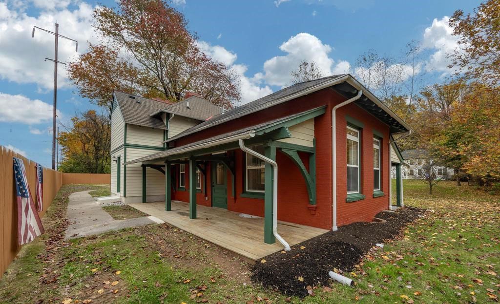 Red building with green trim and covered porch beside a grassy path in autumn