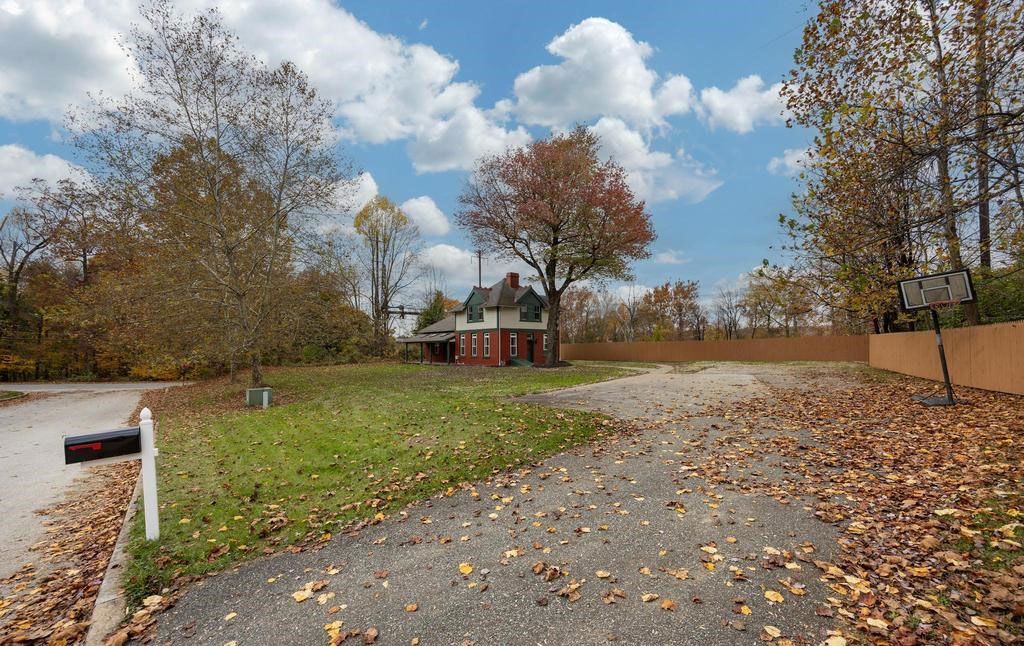 Autumn rural driveway with fallen leaves, a mailbox, and a house under cloudy sky