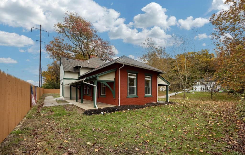 Small red house with a covered porch in a grassy yard under a partly cloudy sky