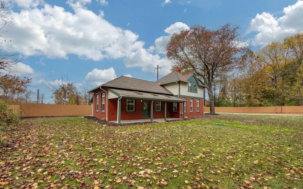 Small red house with white trim in a grassy yard under a cloudy autumn sky