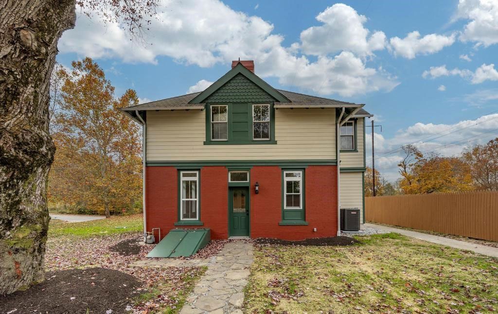 Two-story red and beige house with a front walkway, green trim, and autumn leaves in the yard