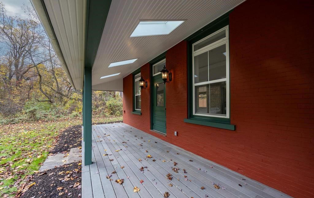 Covered red porch with green door and windows beside a wooded yard in autumn.