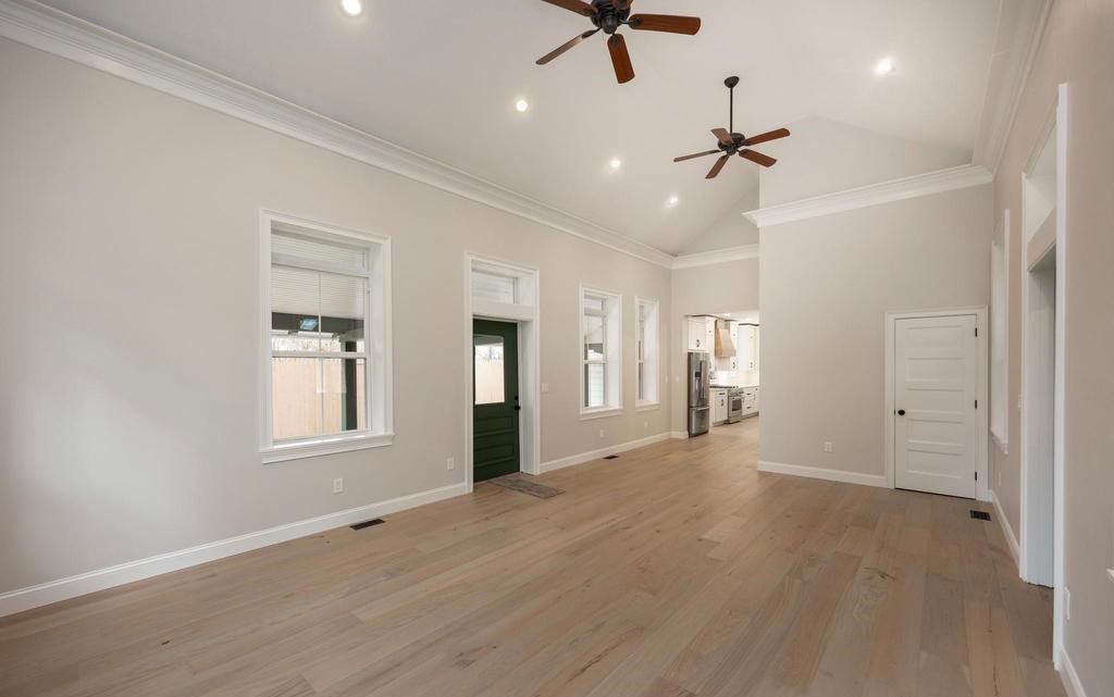 Empty beige room with wood floors, white trim, ceiling fans, and several windows and doors