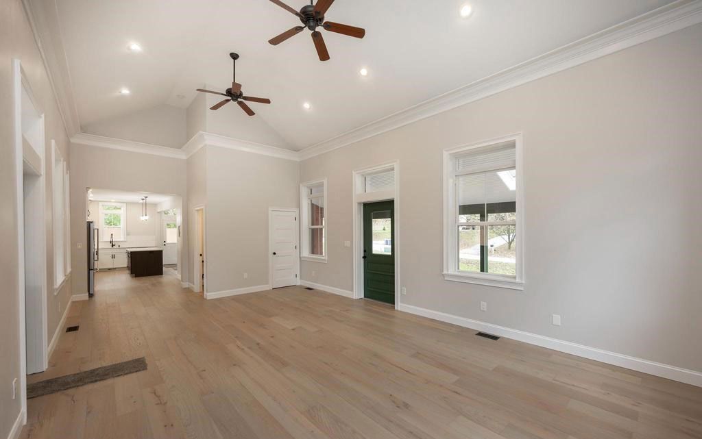 Spacious empty living room with hardwood floors, ceiling fans, large windows, and a dark green front door.