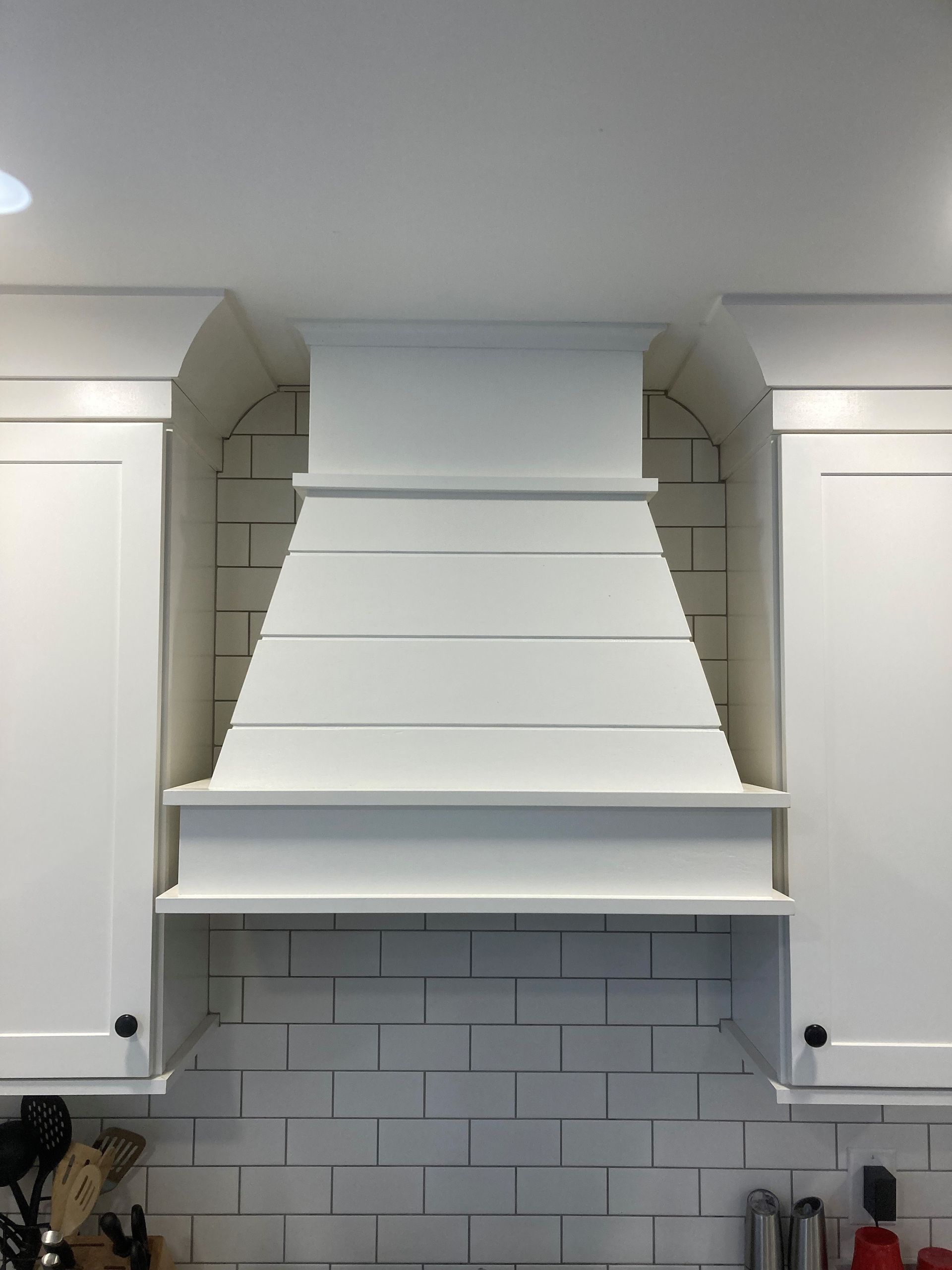 White kitchen range hood flanked by white cabinets over a gray subway tile backsplash