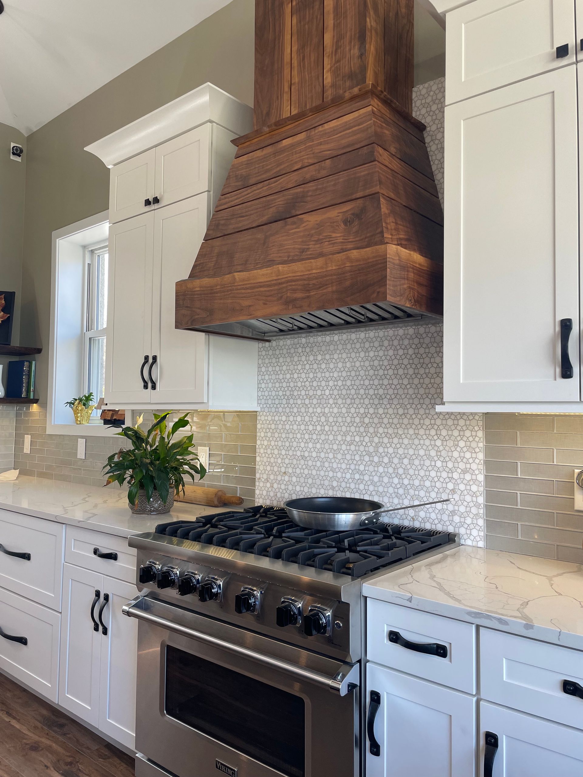 Modern kitchen with white cabinets, marble countertop, stainless range, and a wood range hood over a tiled backsplash