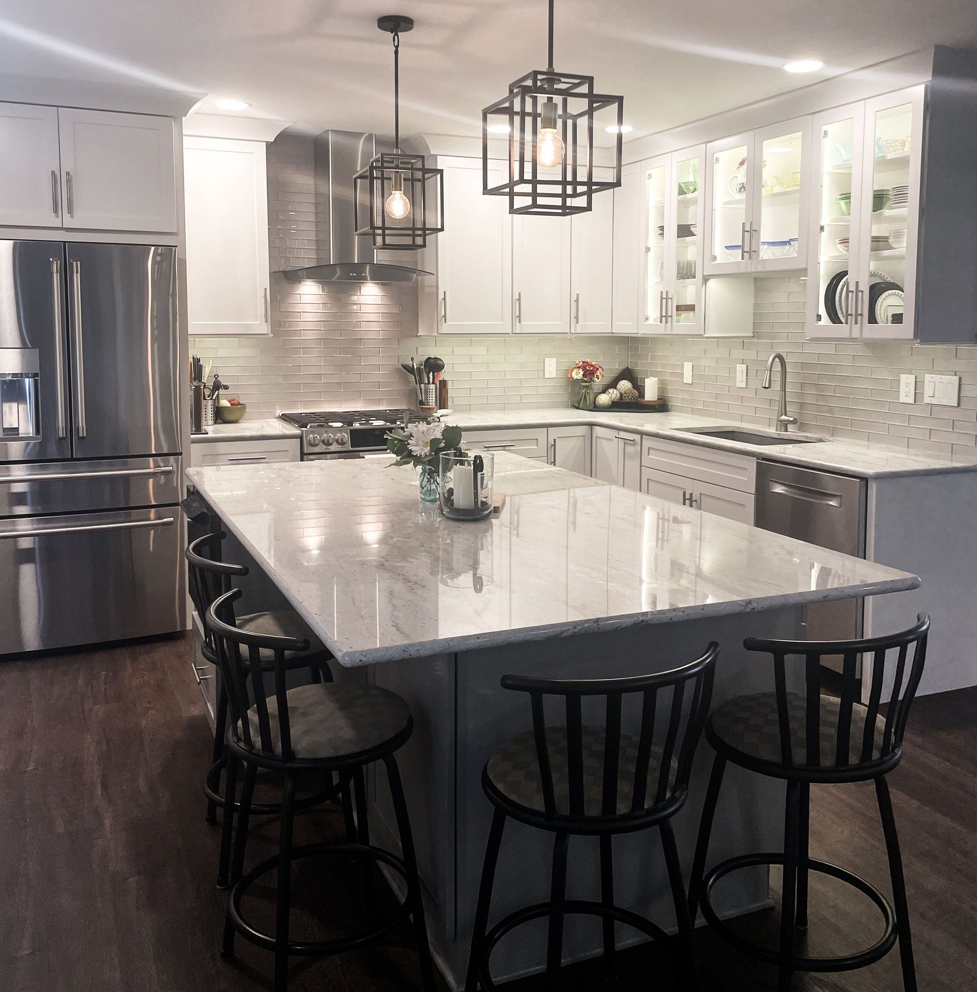 Bright modern white kitchen with marble island, black stools, stainless steel appliances, and hanging pendant lights