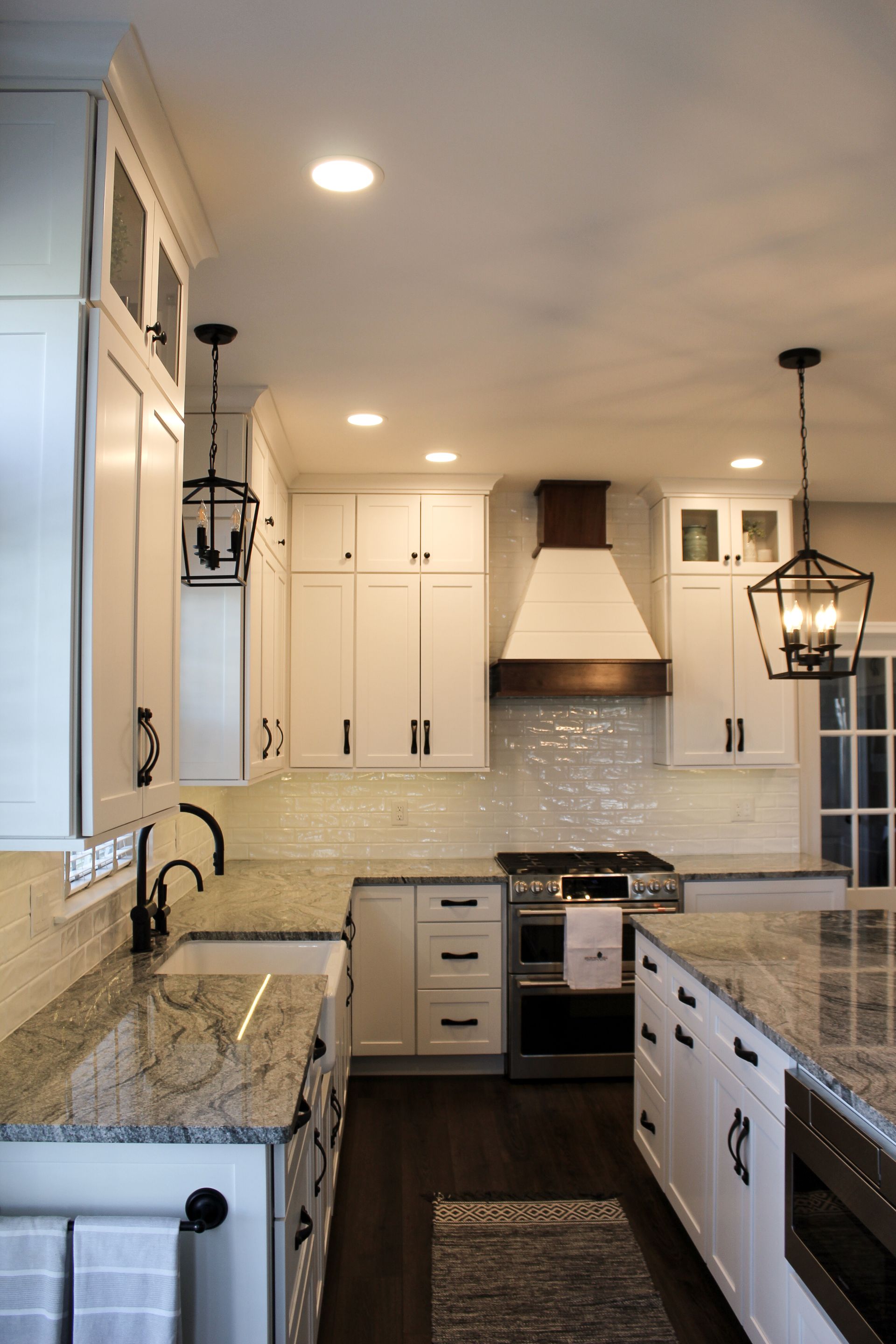 Bright white kitchen with granite counters, stainless appliances, pendant lights, and tiled backsplash