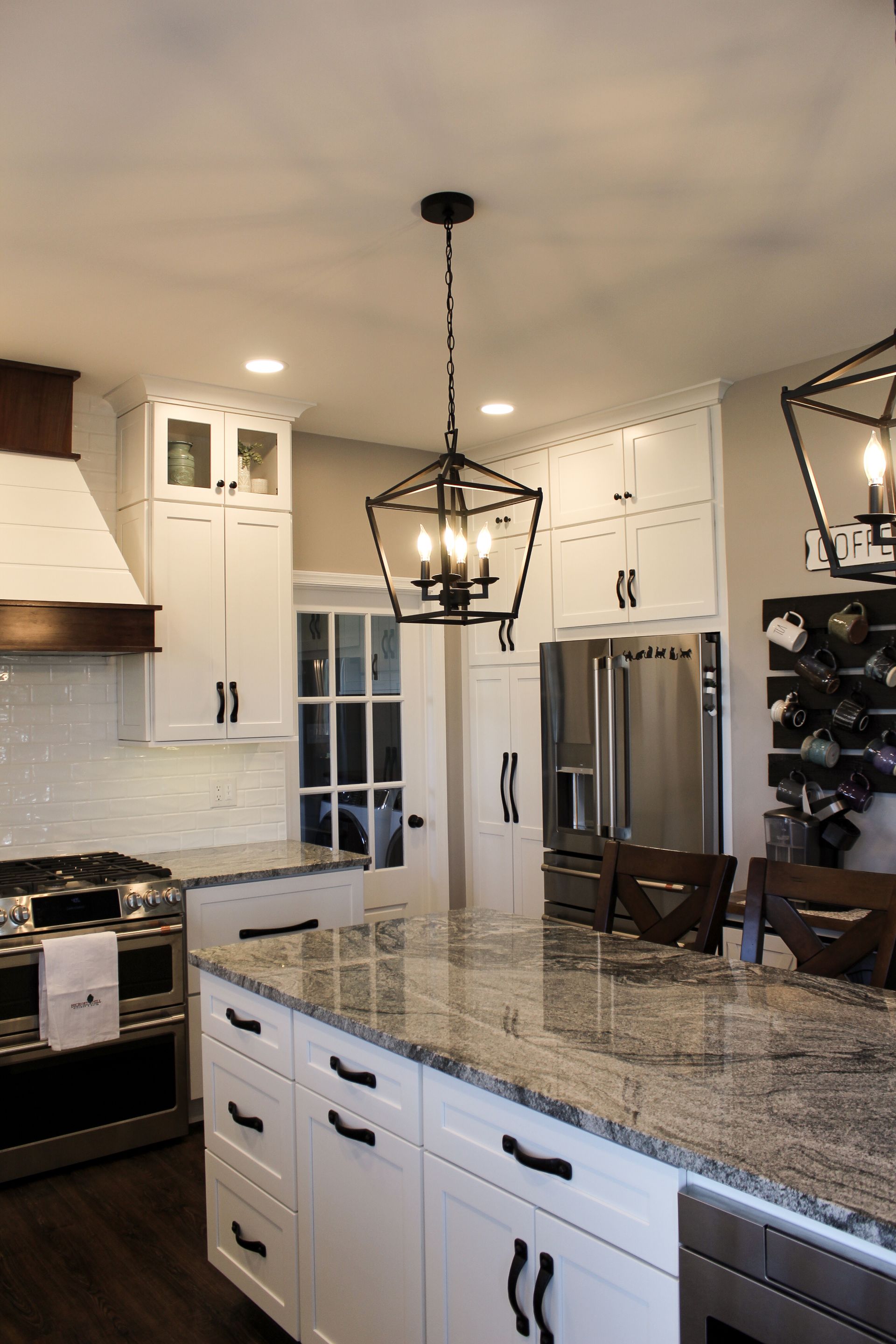 Modern kitchen with white cabinets, granite island, stainless steel appliances, and hanging pendant lights