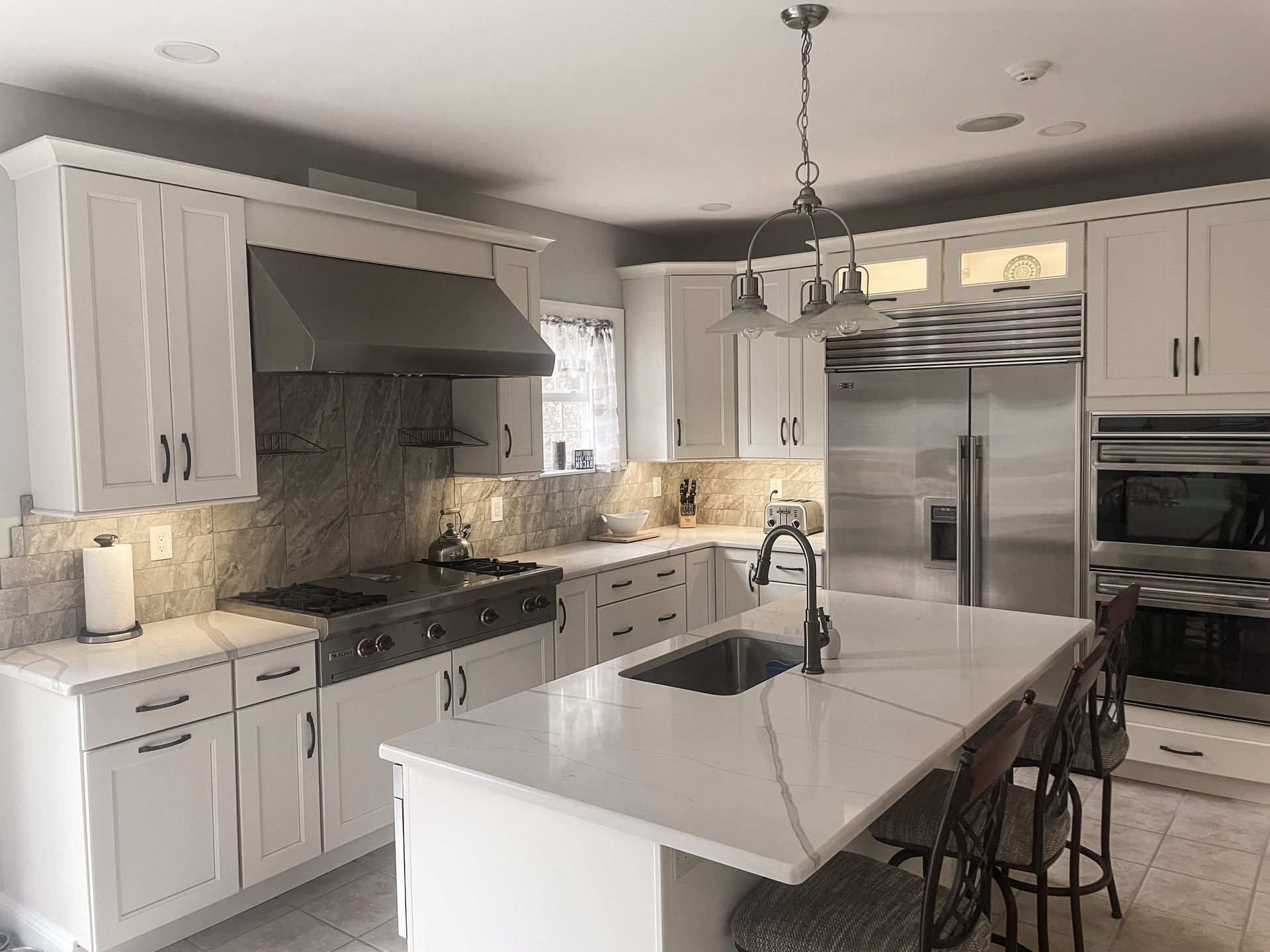 Bright white kitchen with island, stainless steel fridge, farmhouse sink, and pendant lighting
