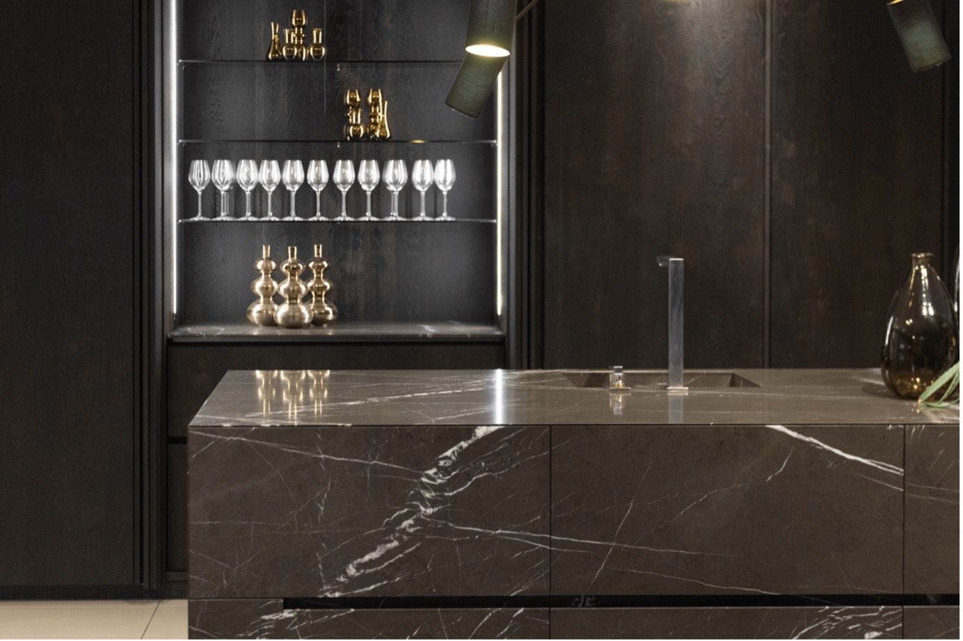 A kitchen with a marble counter top and wine glasses on a shelf