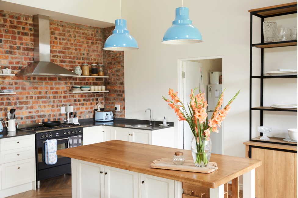 Bright kitchen with brick wall, blue pendant lights, and wooden island with flowers