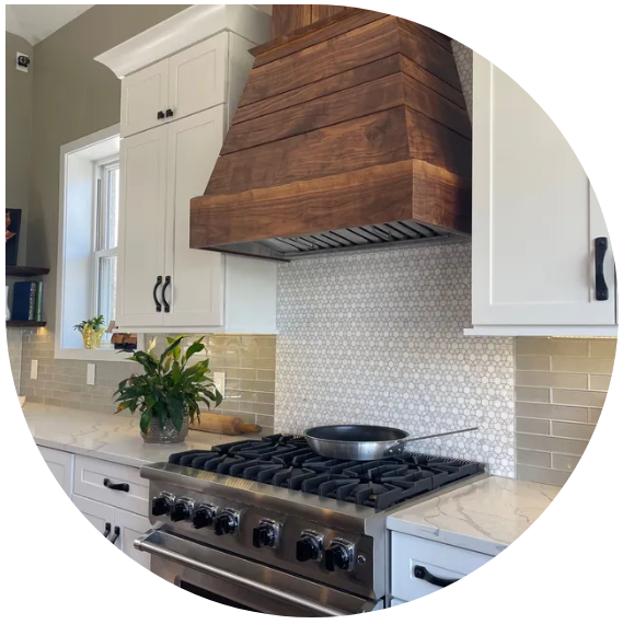 Modern kitchen with wood range hood, stainless stove, white cabinets, and beige tile backsplash