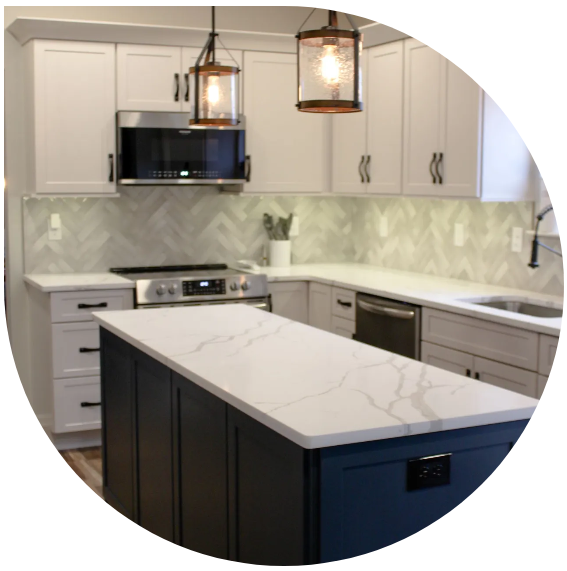 Modern white kitchen with dark island, marble countertops, pendant lights, and stainless-steel appliances