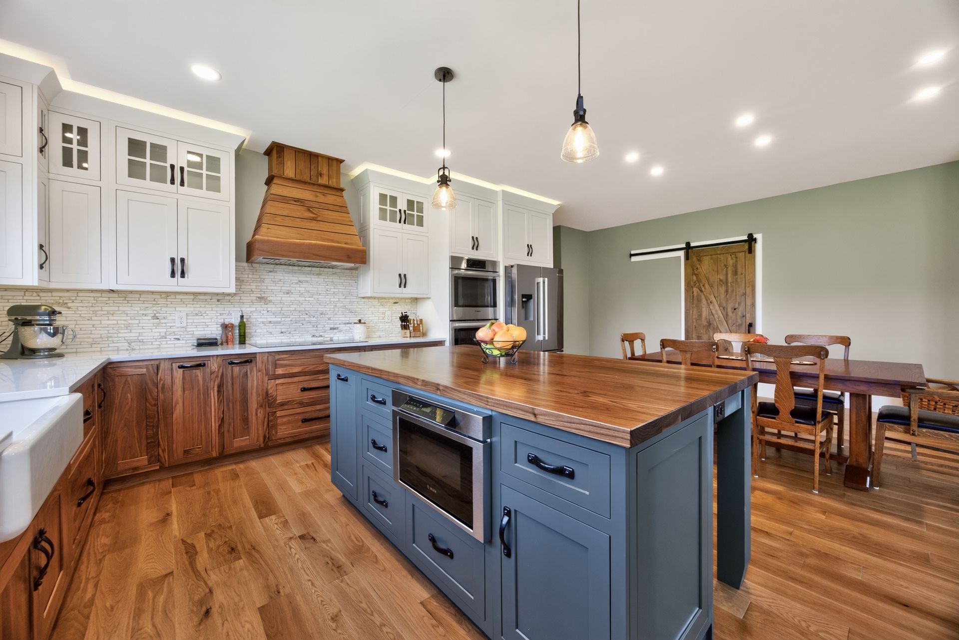 Modern kitchen with wood floors, white cabinets, dark island, and dining area in the background