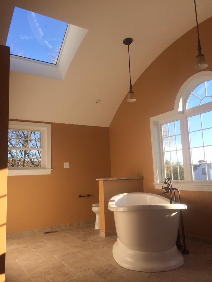 Bright bathroom with a freestanding tub, skylight, arched window, and tan walls