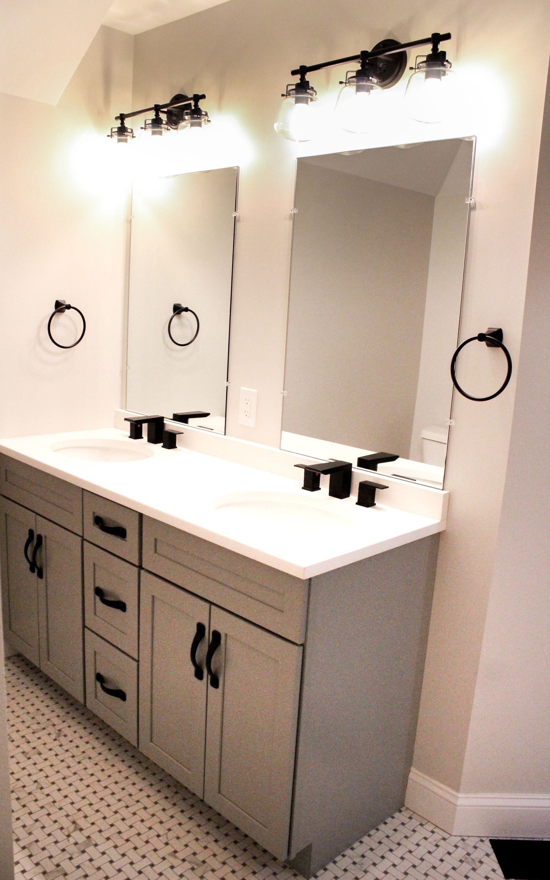 Modern bathroom vanity with double mirrors, white countertop, and dark wood cabinets under wall lights