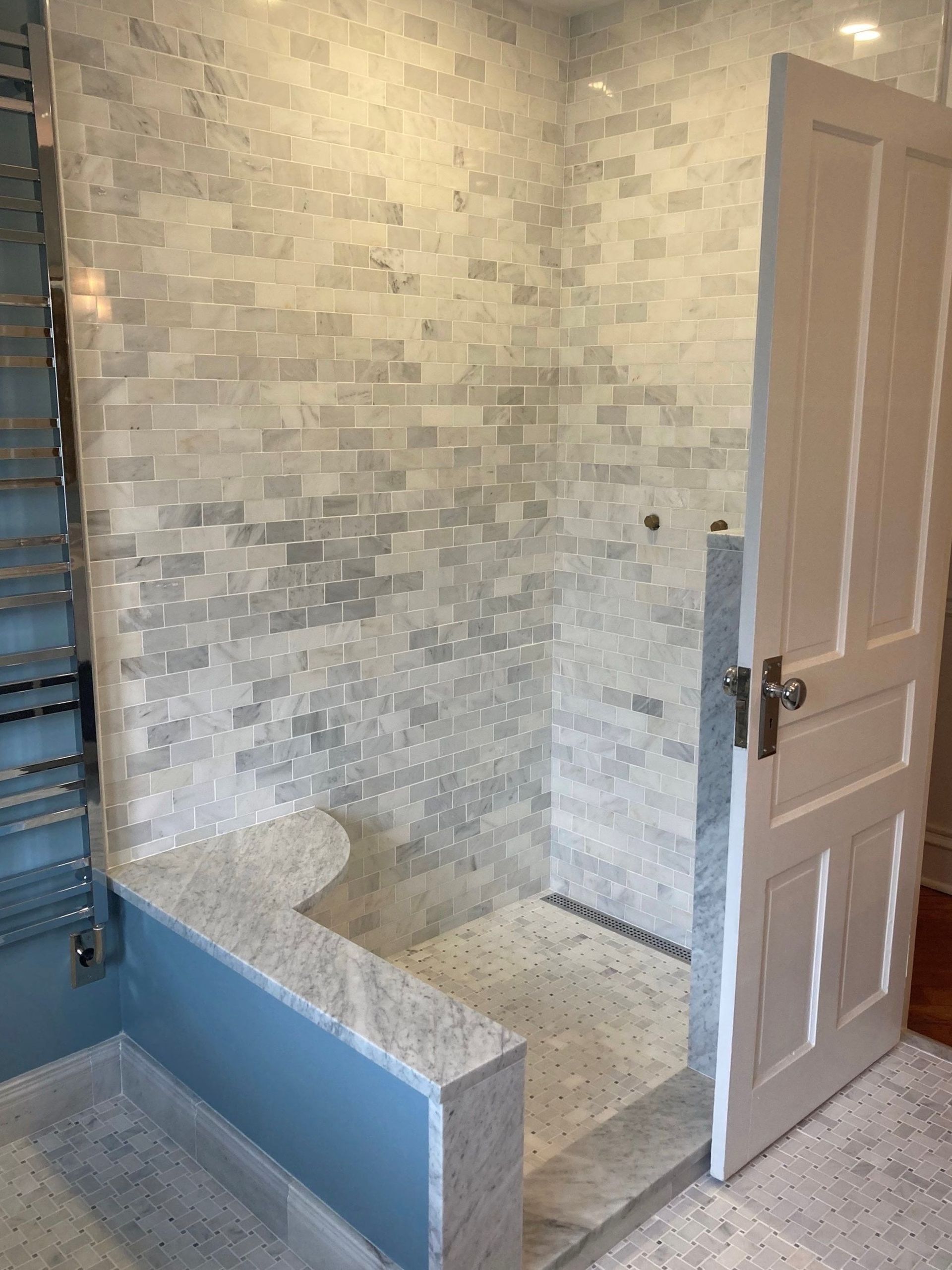 Tiled bathroom with a walk-in shower, white bench, and an open door.