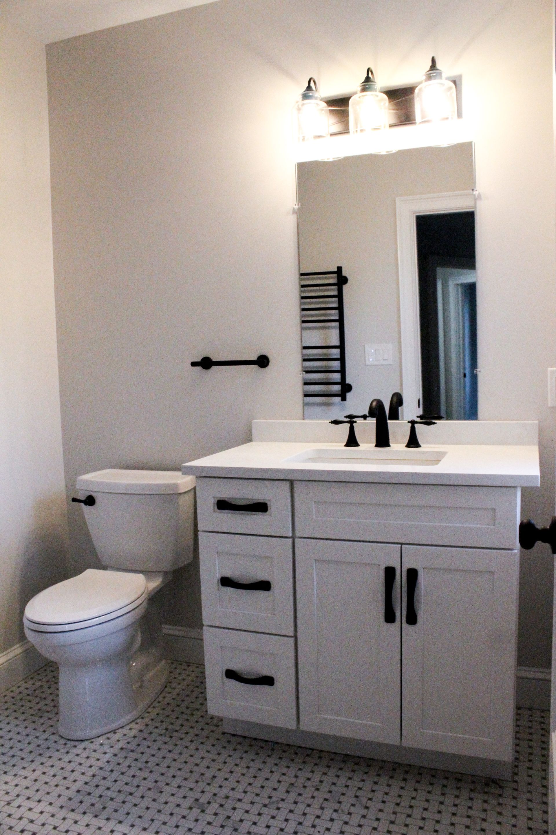 Small modern bathroom with a white vanity, mirror, sink, toilet, and black fixtures