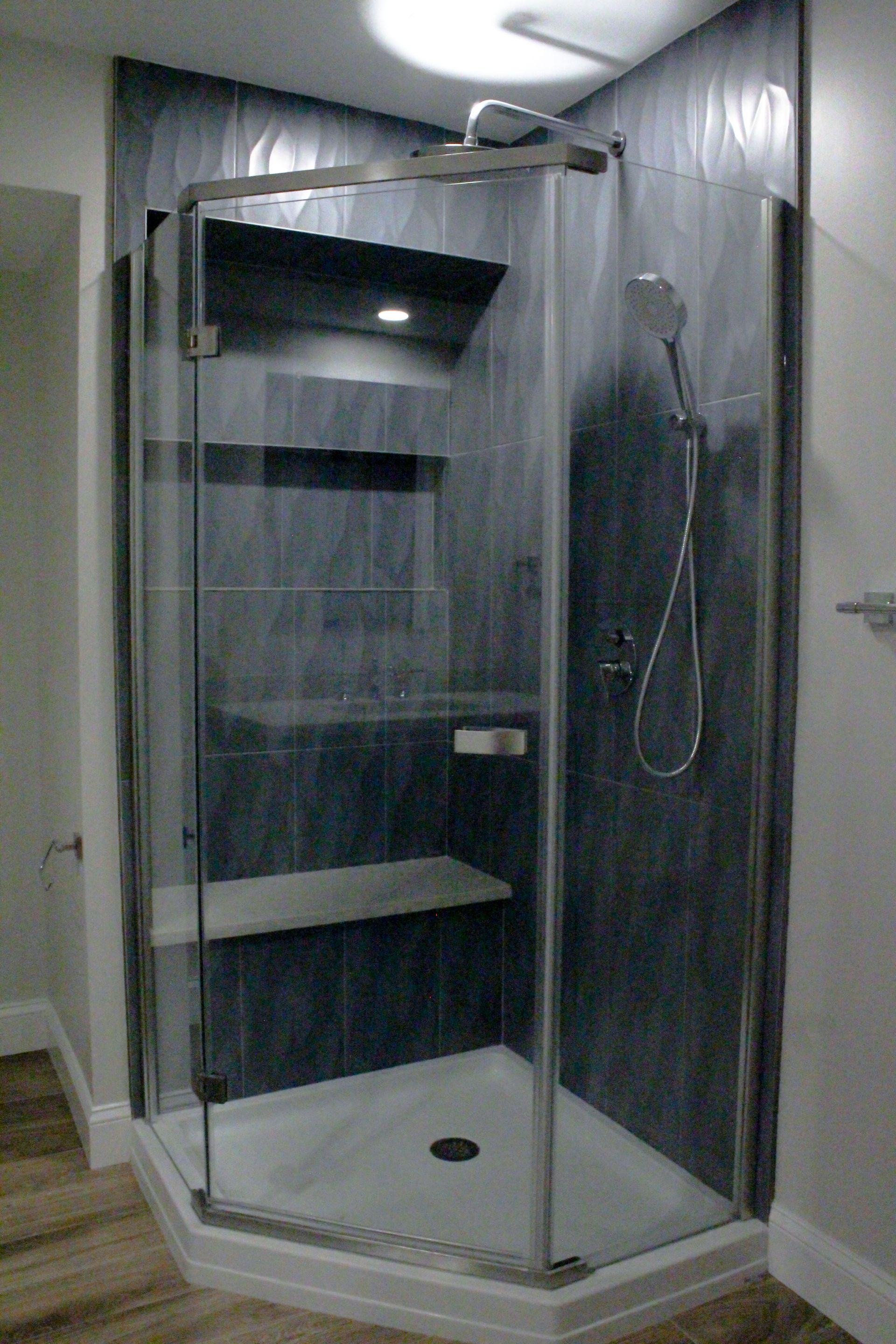 Corner glass shower stall with built-in shelves and handheld showerhead in a small bathroom