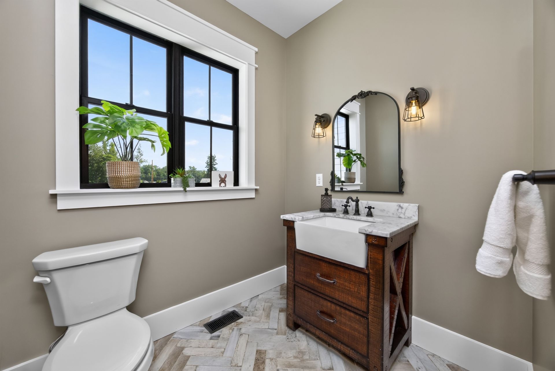 Small bathroom with window, white toilet, wood vanity, mirror, and beige walls.
