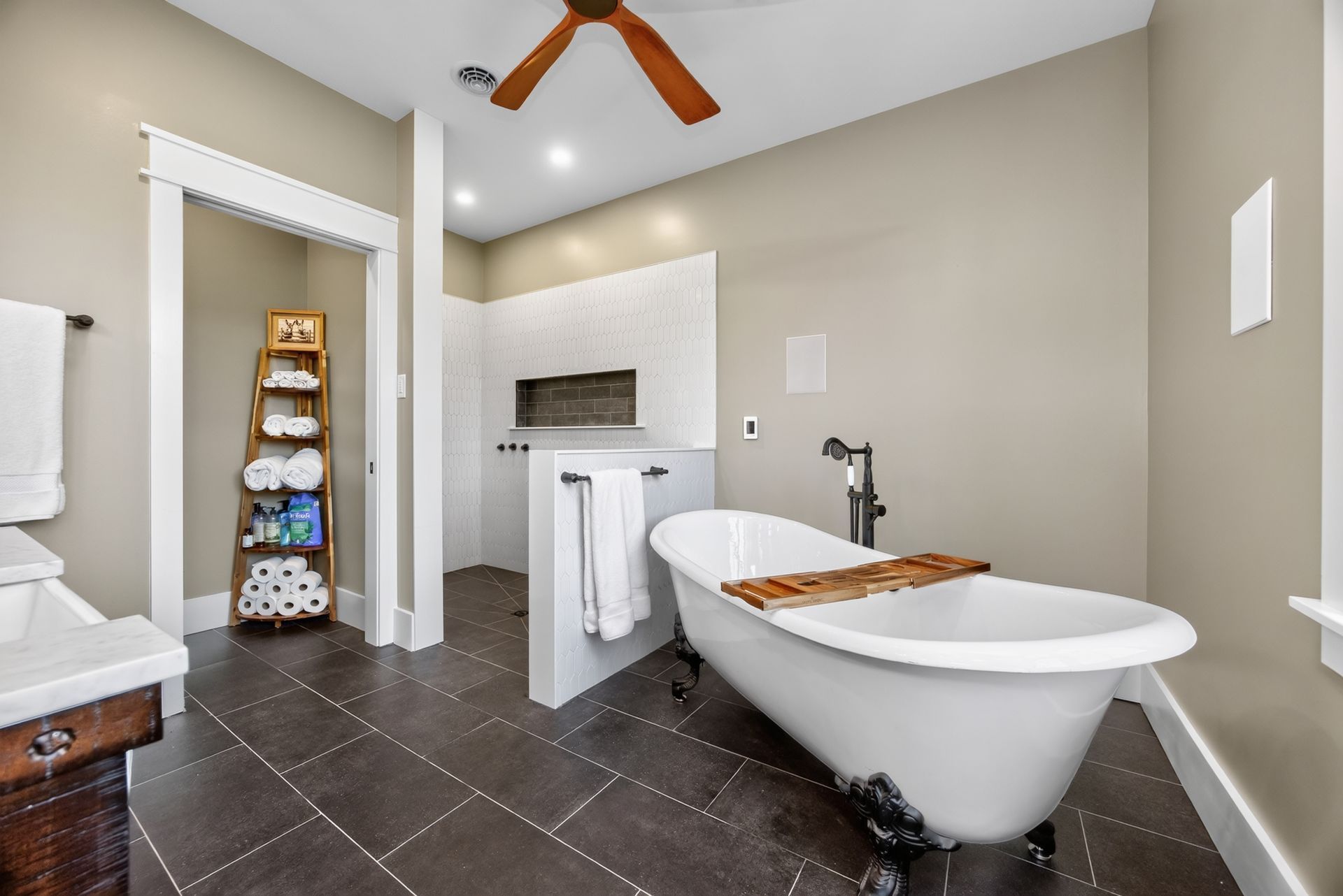 Modern bathroom with freestanding tub, dark tile floor, vanity, and towel shelves