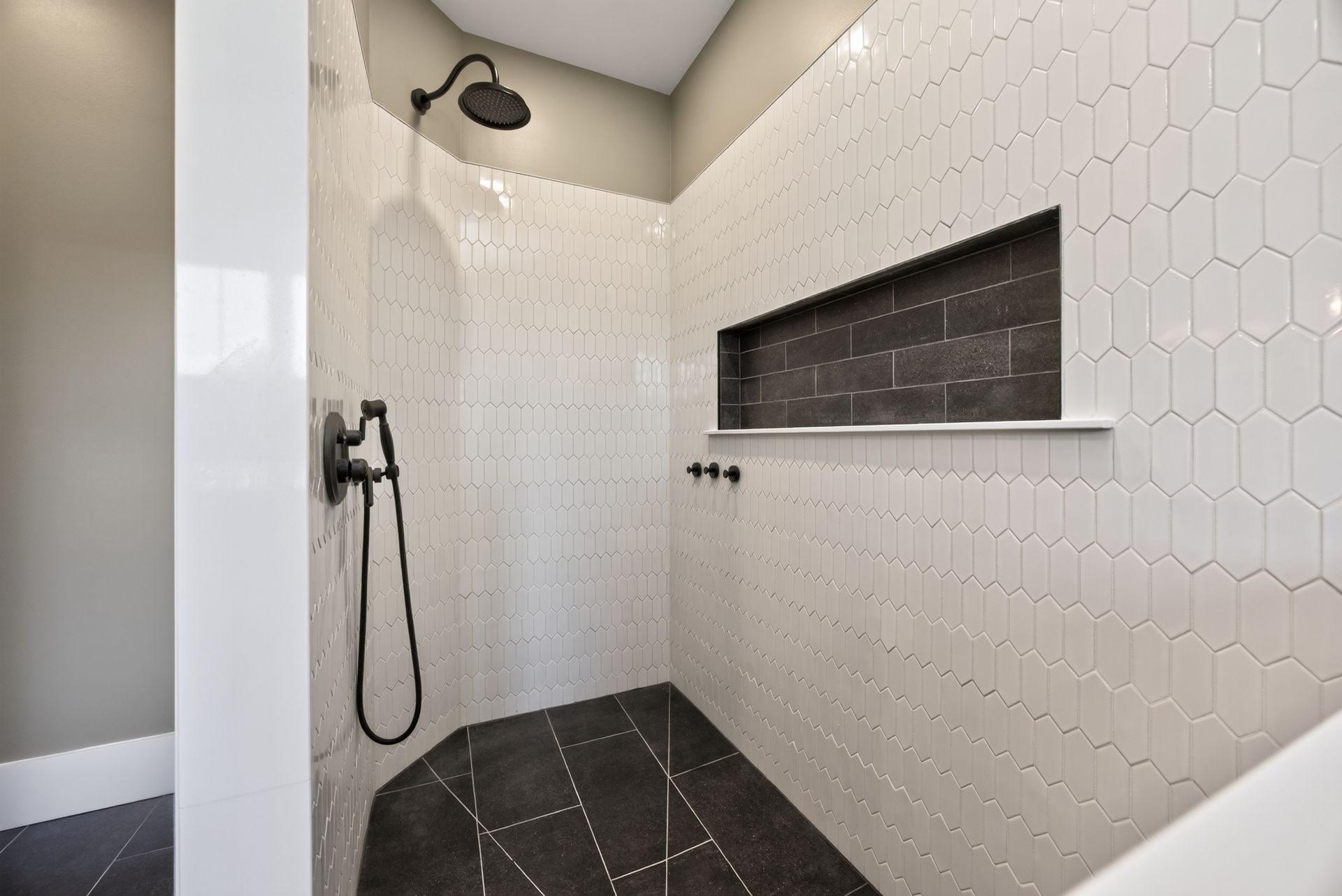 Modern tiled walk-in shower with black fixtures, overhead rain shower, and built-in shelf