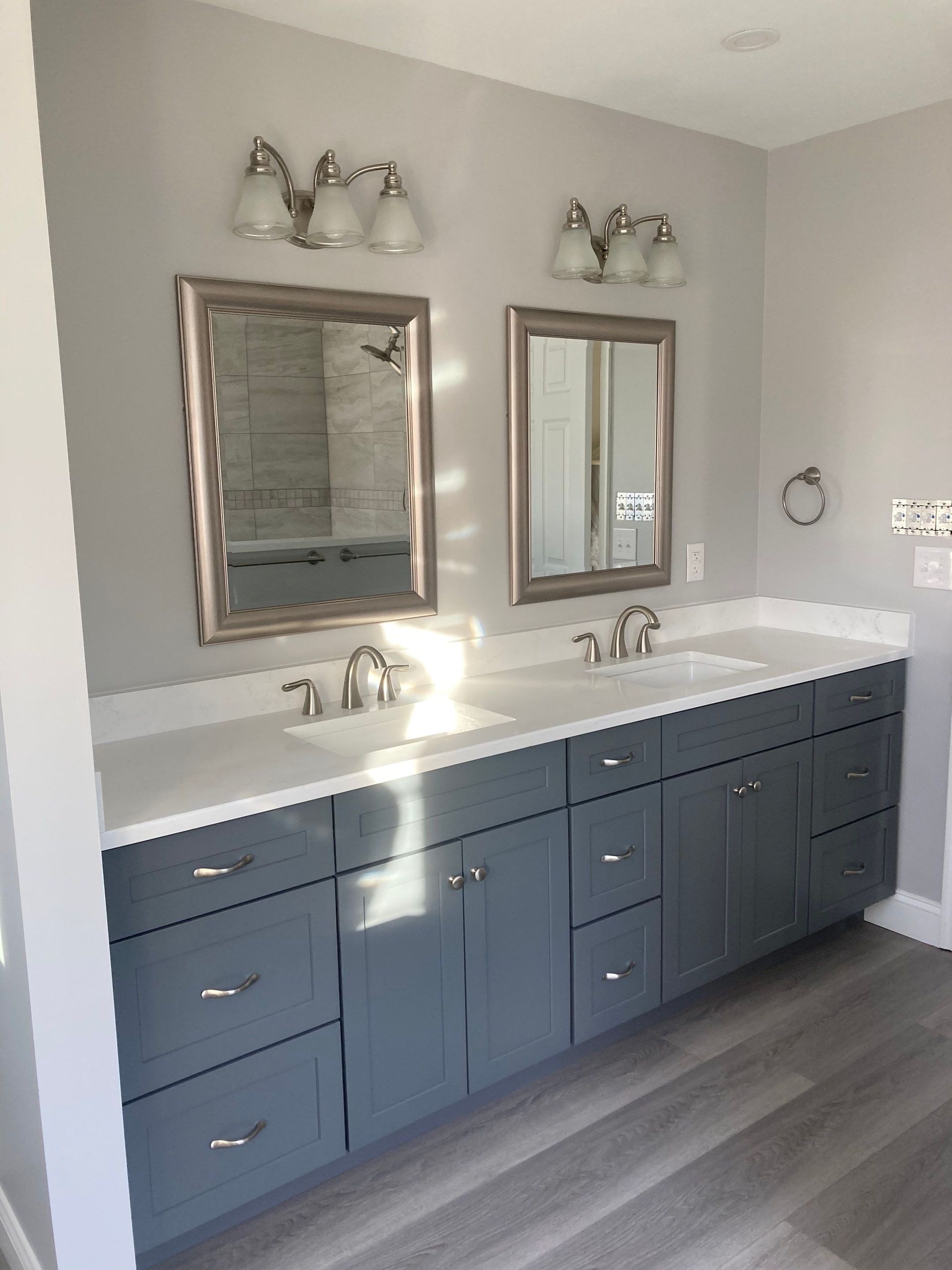 Modern bathroom vanity with double sinks, blue cabinets, two mirrors, and gray flooring.