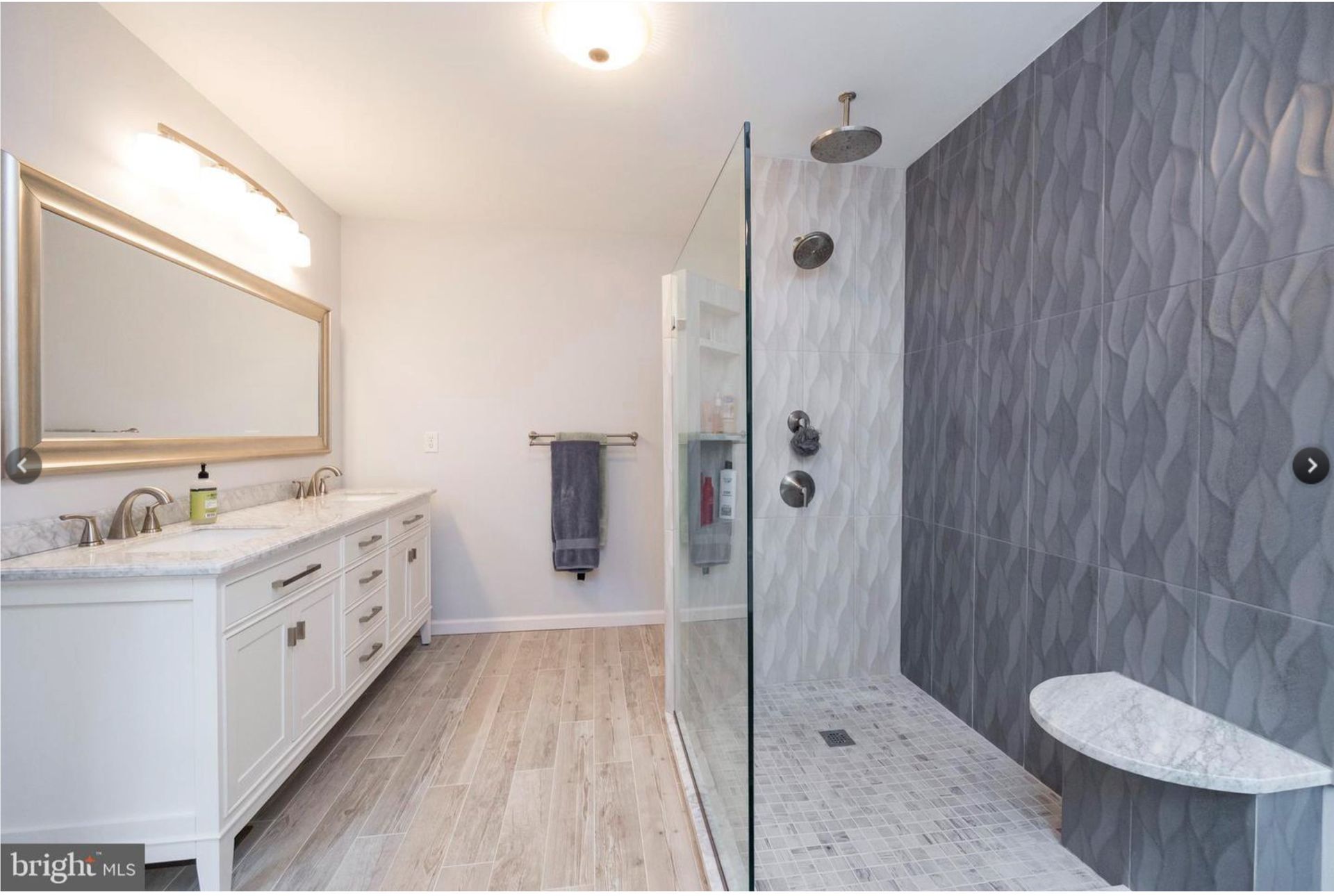 Bright bathroom with white vanity, large mirror, wood-look floor, and glass shower beside a dark textured accent wall