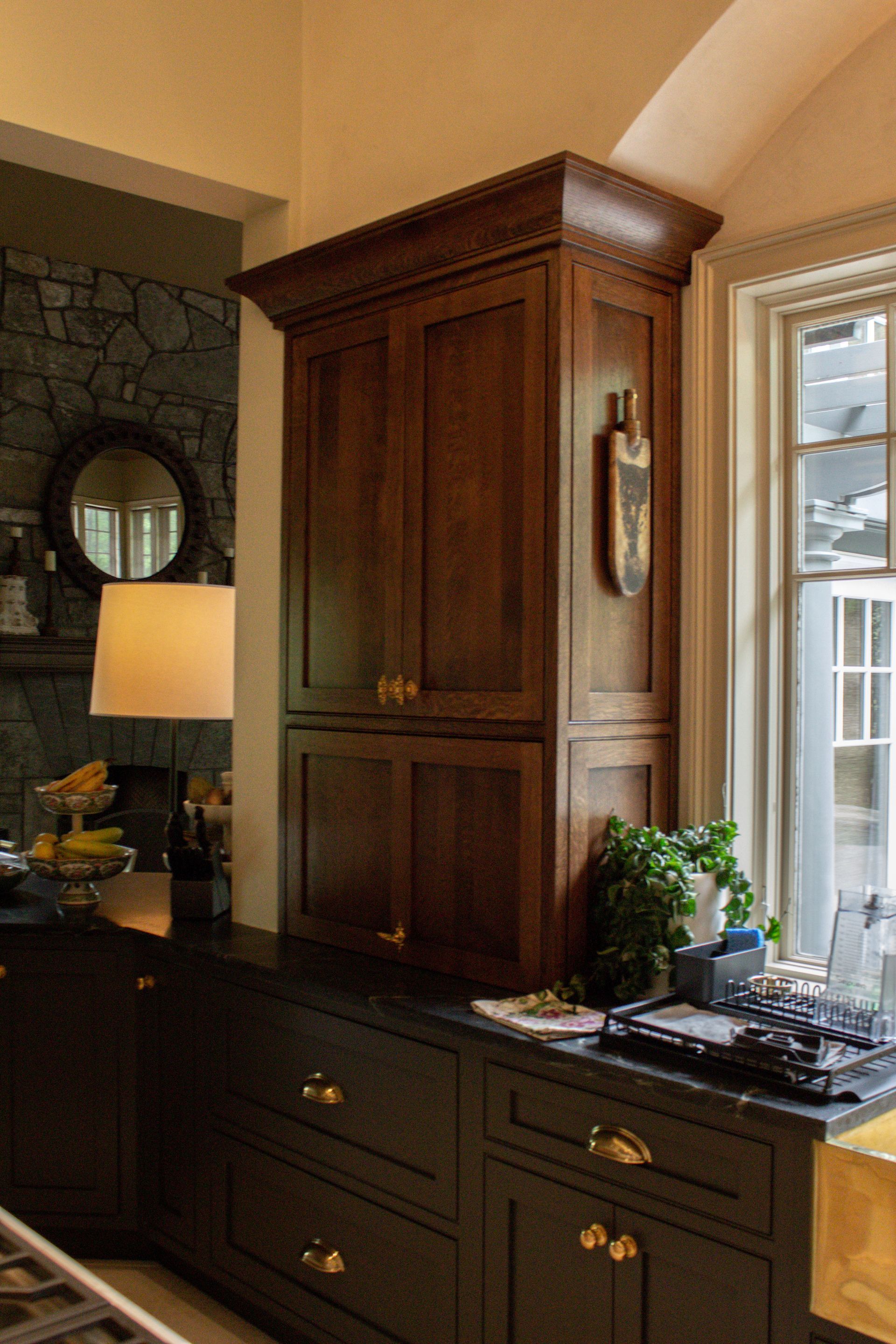 Wooden cabinet above dark dresser beside a sunlit window in a cozy room