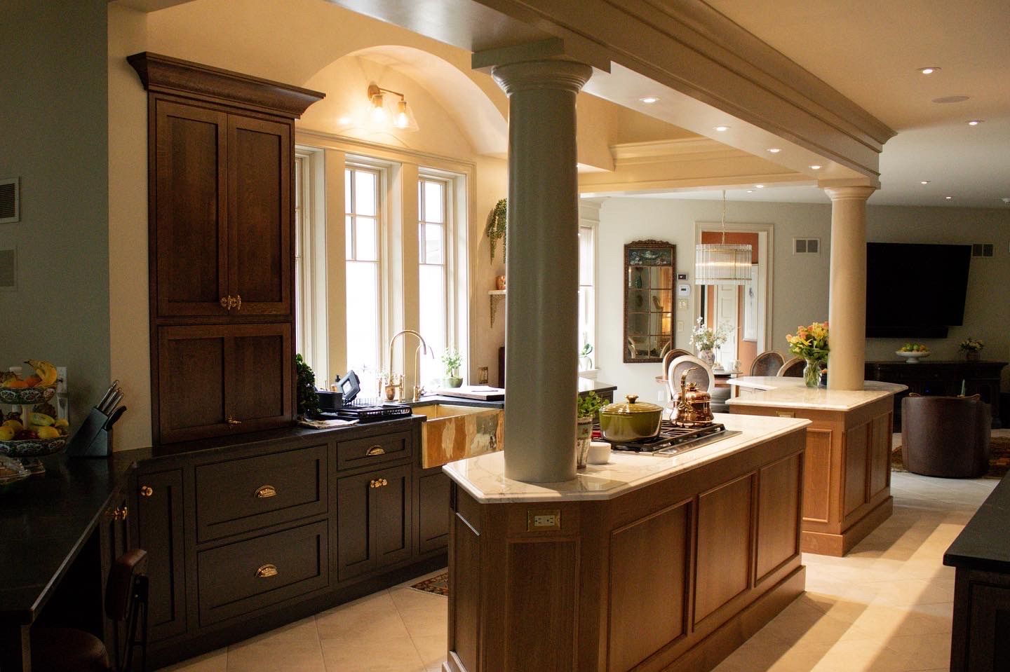Bright kitchen with dark cabinets, island, and warm lighting overlooking a living room