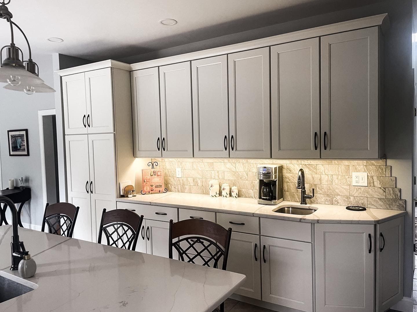 Modern kitchen with white cabinets, marble island, and under-cabinet lighting under a dark ceiling