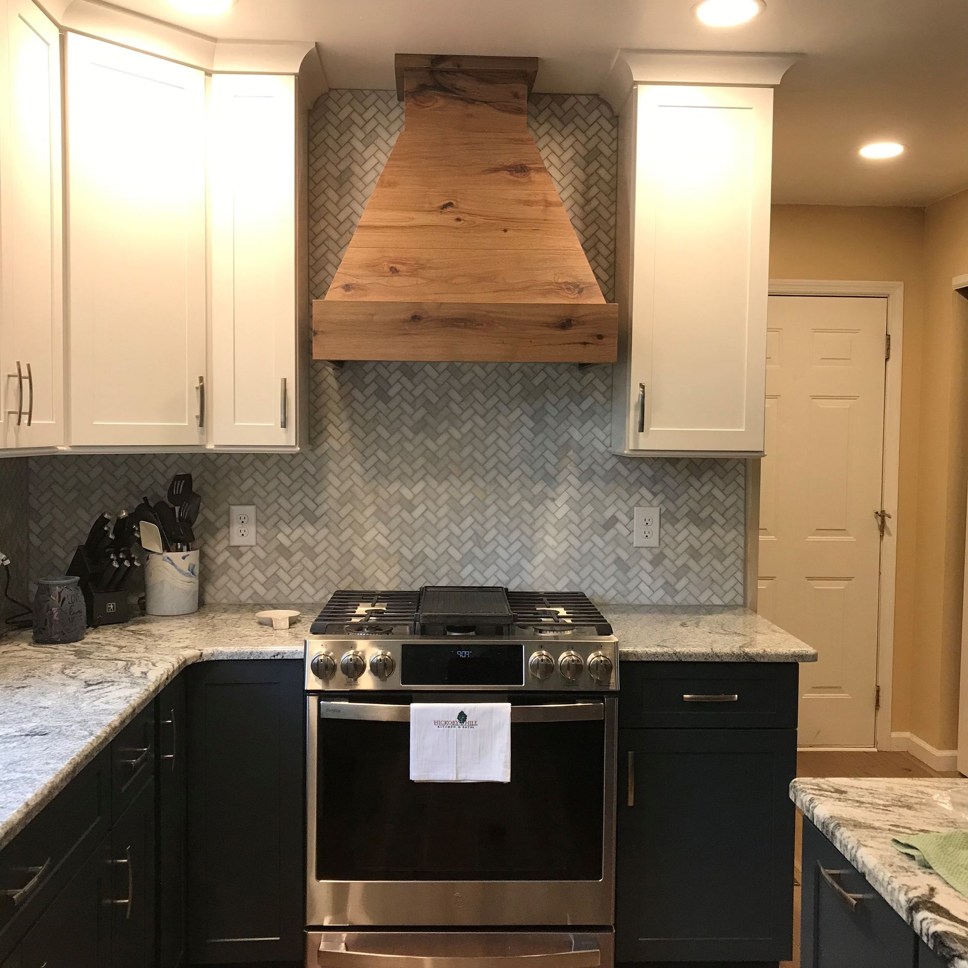 Modern kitchen with white cabinets, dark lower cabinets, granite counters, stainless stove, and wood range hood