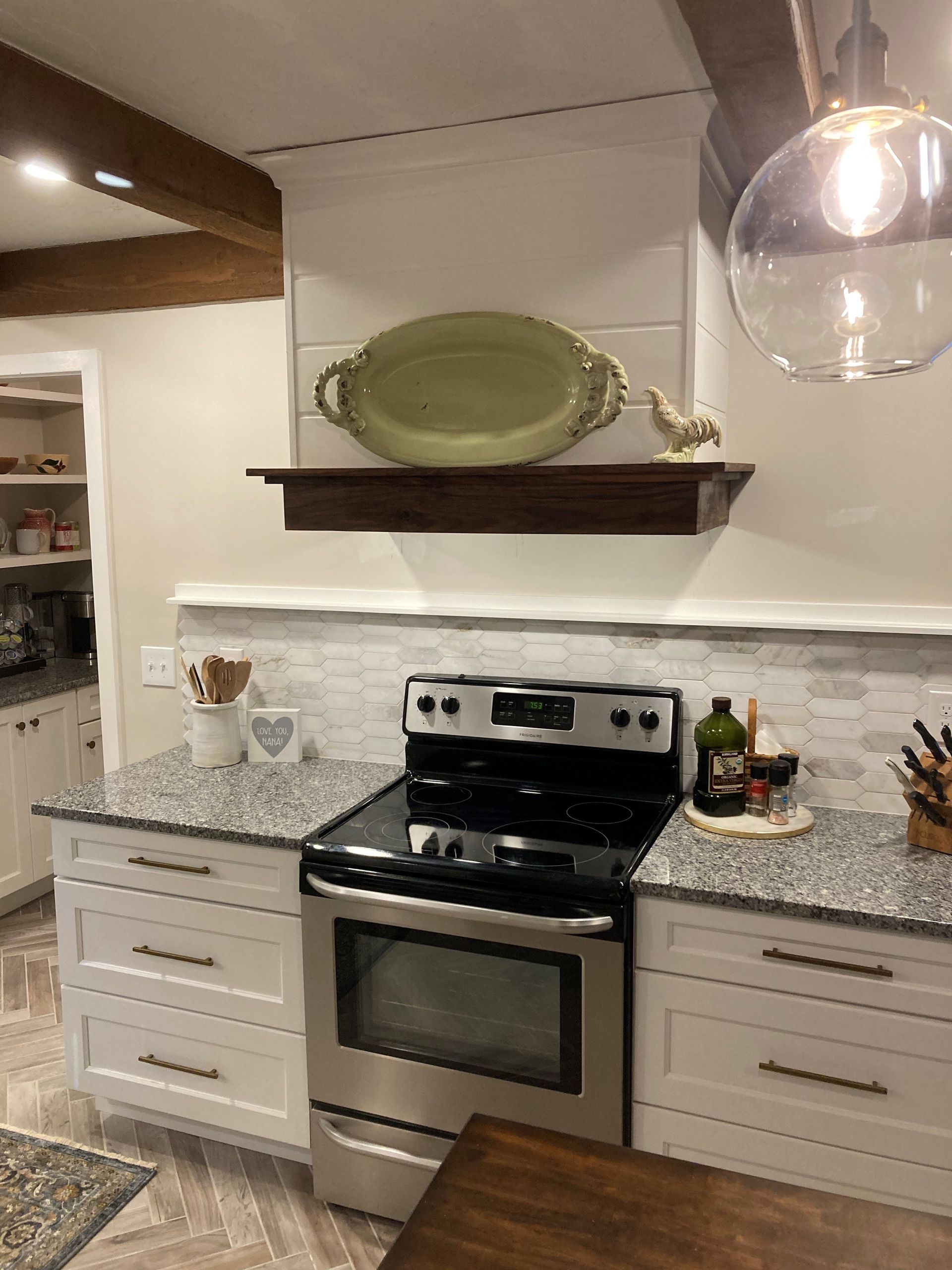 Kitchen with stainless steel stove, speckled countertops, white cabinets, and a decorative shelf above the range