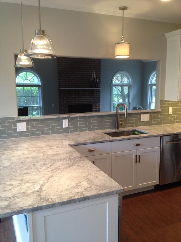 Modern kitchen with gray island, pendant lights, tiled backsplash, and double sink overlooking arched windows.