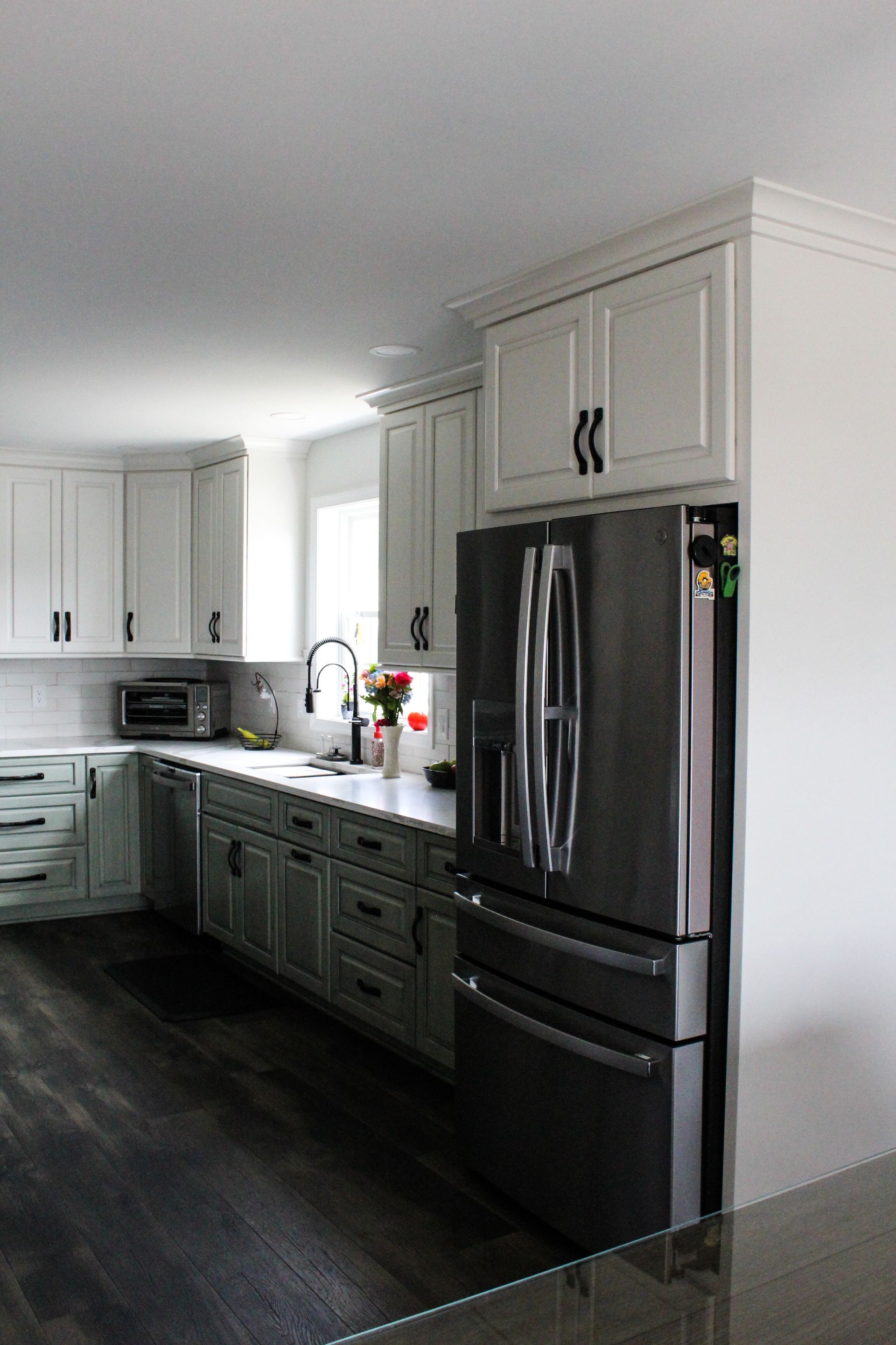 Modern kitchen with white cabinets, dark lower cabinets, stainless steel fridge, and dark wood flooring