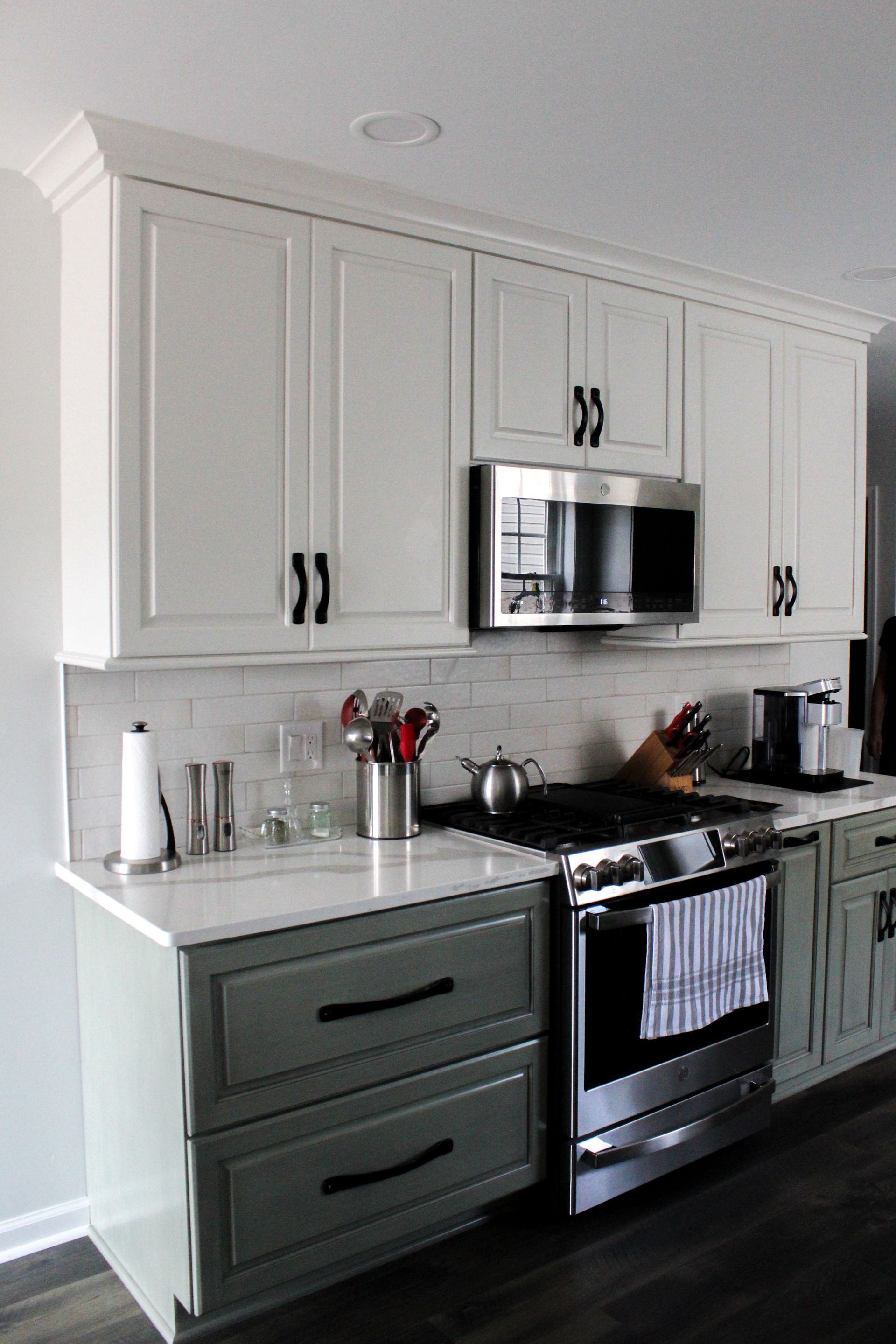Modern kitchen with white cabinets, green lower drawers, stainless steel appliances, and dark wood flooring