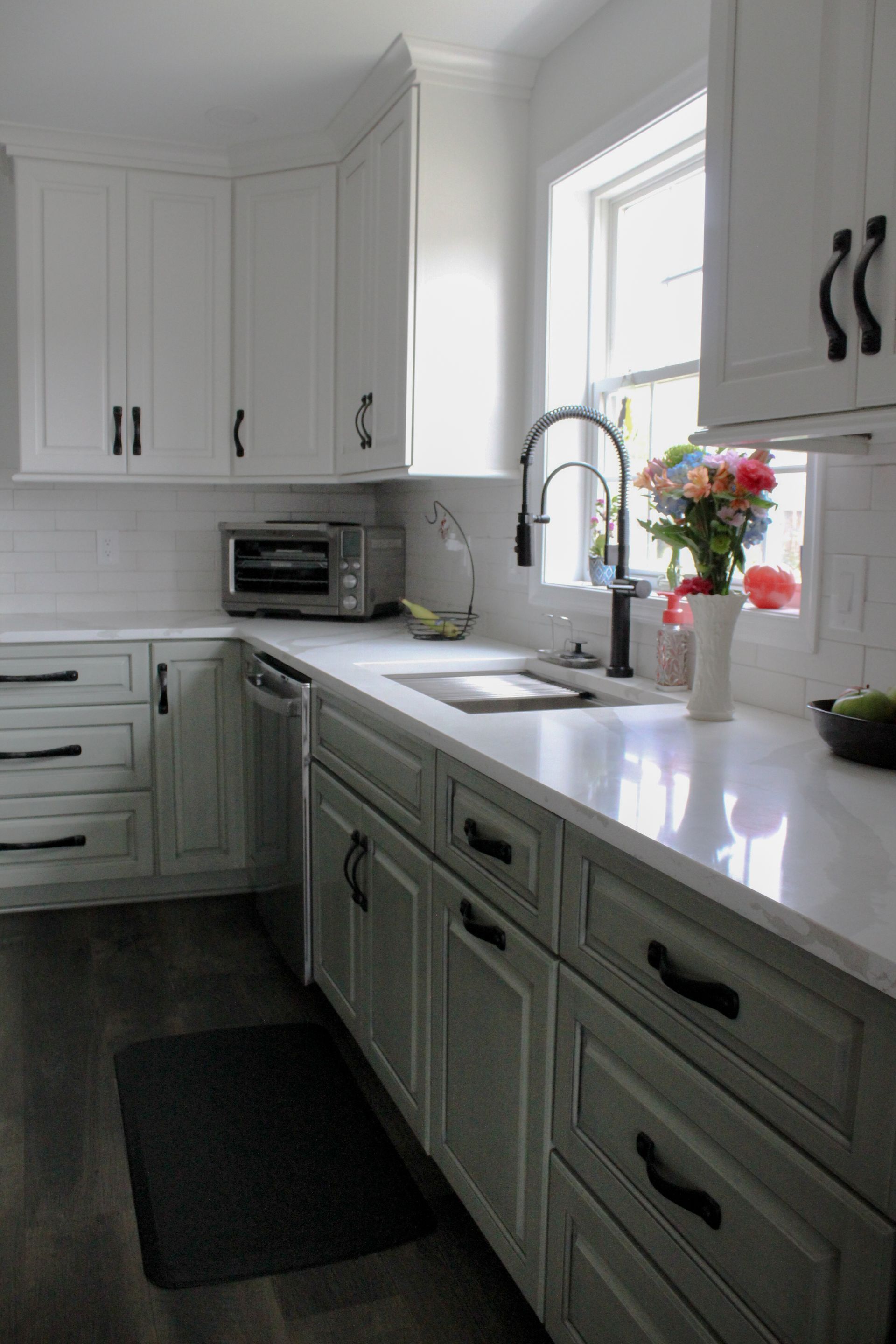 Bright white kitchen with green cabinets, a sink by a window, and flowers on the counter.